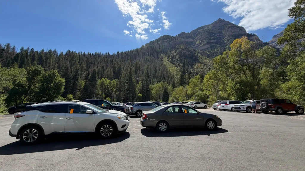 Three cars parked outside of marked parking spaces in a large lot have an orange ticket in their window.